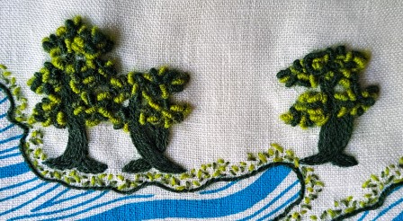 Gros plan sur 3 arbres brodés. Le tronc est brodé simplement en vert foncé et le feuillage avec des points noués en relief dans 3 nuances de vert.