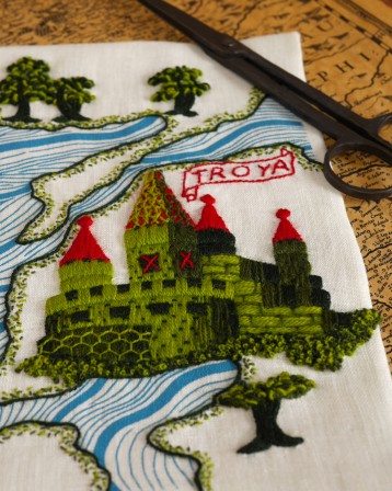 Détail de la broderie centré sur la cité brodée en vert avec des toits rouges sur plusieurs tours. Au dessus un cartel en forme de parchemin où il est écrit &amp;quot;Troya".