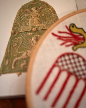 detail de la broderie des ailes du dragon, en rouge. la broderie est posée sur un livre avec la photo d'une broderie médiévale où un ange a le meme style d'ailes