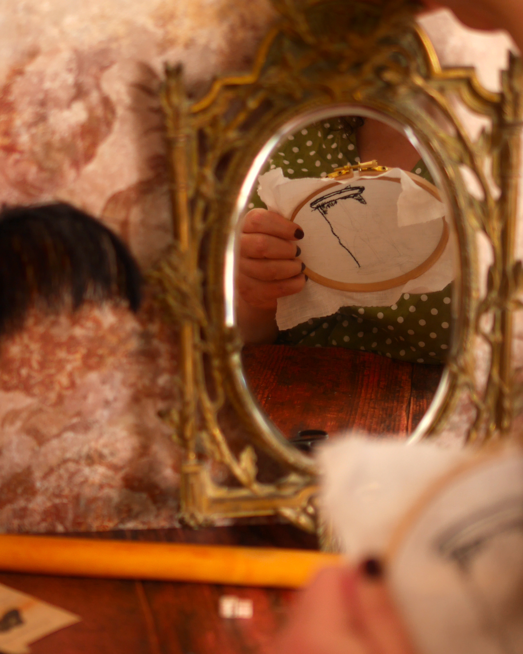 Personne en train de broder qu'on aperçoit dans un miroir dévoilant l'envers de la broderie.