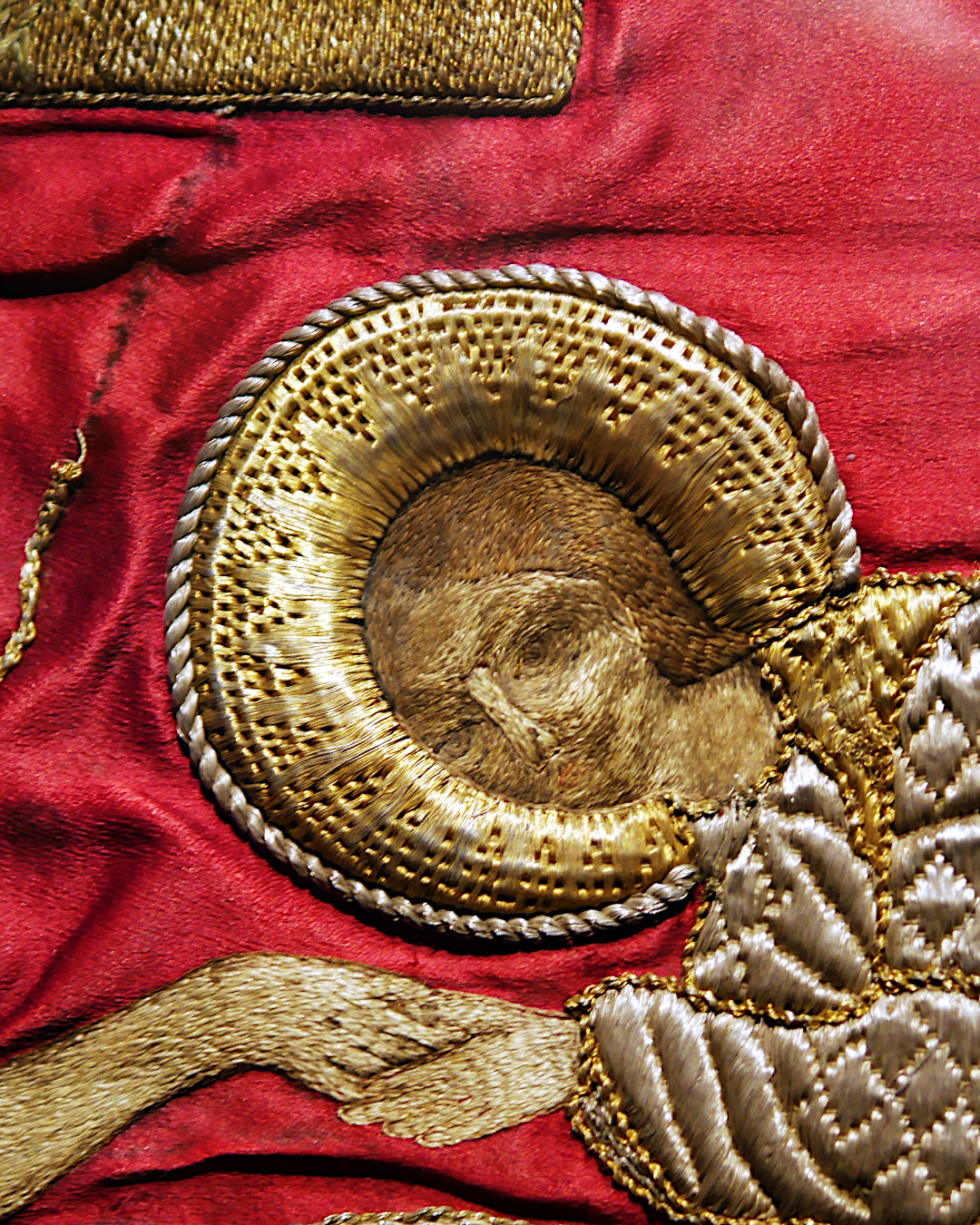 Détail de la broderie de la tête d'un autre personnage, un homme auréolé. L'auréole est brodée au fil d'or avec différentes textures qui forment un &amp;quot;soleil". Son manteau est brodé en soie mais avec le même genre de texture que la broderie d'or.
