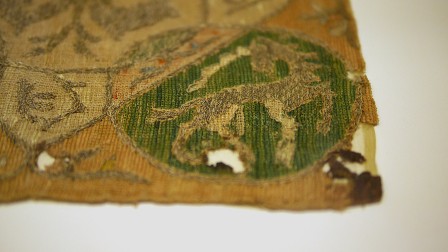 Détail de la broderie d'une aumônière du moyen-âge. On voit un médaillon contenant une licorne brodée au fil d'or. Tout le fond est brodé de points de chaînettes en lignes parallèles collées pour faire le remplissage