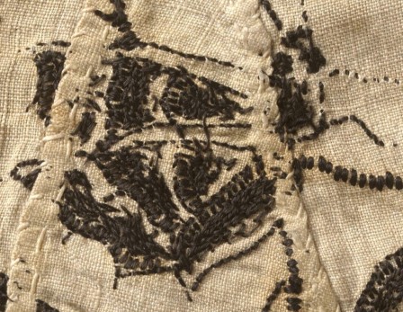 Détail de l'envers d'une veste brodée en noir sur toile blanche. On distingue vaguement la forme d'un papillon. Aucun fil ne traine mais on ne peut pas deviner le détail des points sur l'endroit.
