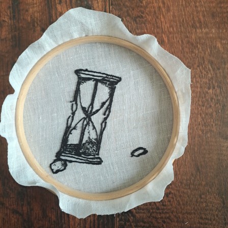 Broderie vue sur l'envers. C'est un sablier brodé en noir sur toile blanche. On distingue bien la forme générale mais l'envers est brouillon, on voit bien que ce n'est pas le côté &amp;quot;fini&quot;.