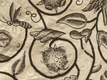 Détail d'une broderie au fil noir sur toile écrue. La broderie est un décors mélangeant végétaux et animaux dans le style des gravures. Les tiges qui forment un décors sont brodées avec un point plus épais