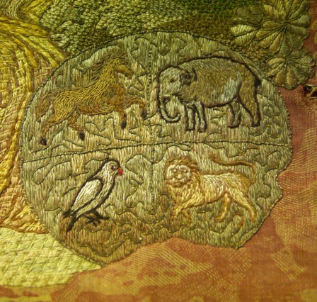 Détail de la broderie sur un disque séparé en 4 quarts dont le fond est brodé en gris. Sur chaque partie, un animal : cheval, éléphant, lion et perroquet.