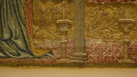 Détail d'une broderie. Le sol est brodé au fil d'or avec une couchure rouge en forme de losanges.