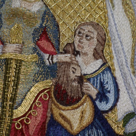 Détail de la broderie de la servante brodée aux fils de soie colorée. Elle regarde vers Judith. Elle porte une robe bleu. Elle tend un sac en toile beige. On voit également la tête d'Holopherne, brune avec une barbe et quelques gouttes de sang qui s'écoulent de son cou