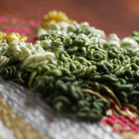 Détail de la broderie du feuillage d'un arbre. C'est un point de broderie qui crée un volume un peu chaotique avec des fils entortillés sur eux-mêmes.