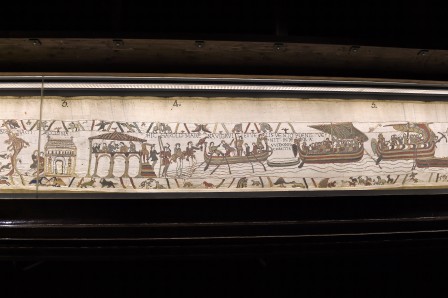 Photo d'une partie de la tapisserie de Bayeux dans le musée, on voit des bâtiments et des bâteaux